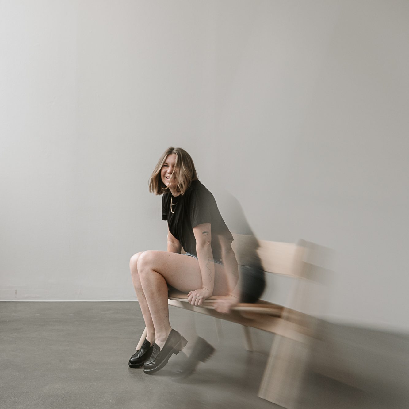 Eine Person sitzt lachend auf einem Stuhl. Das Bid wurde in Bewegung aufgenommen, als ob die Person gerade mit Schwung aufstehen möchte.