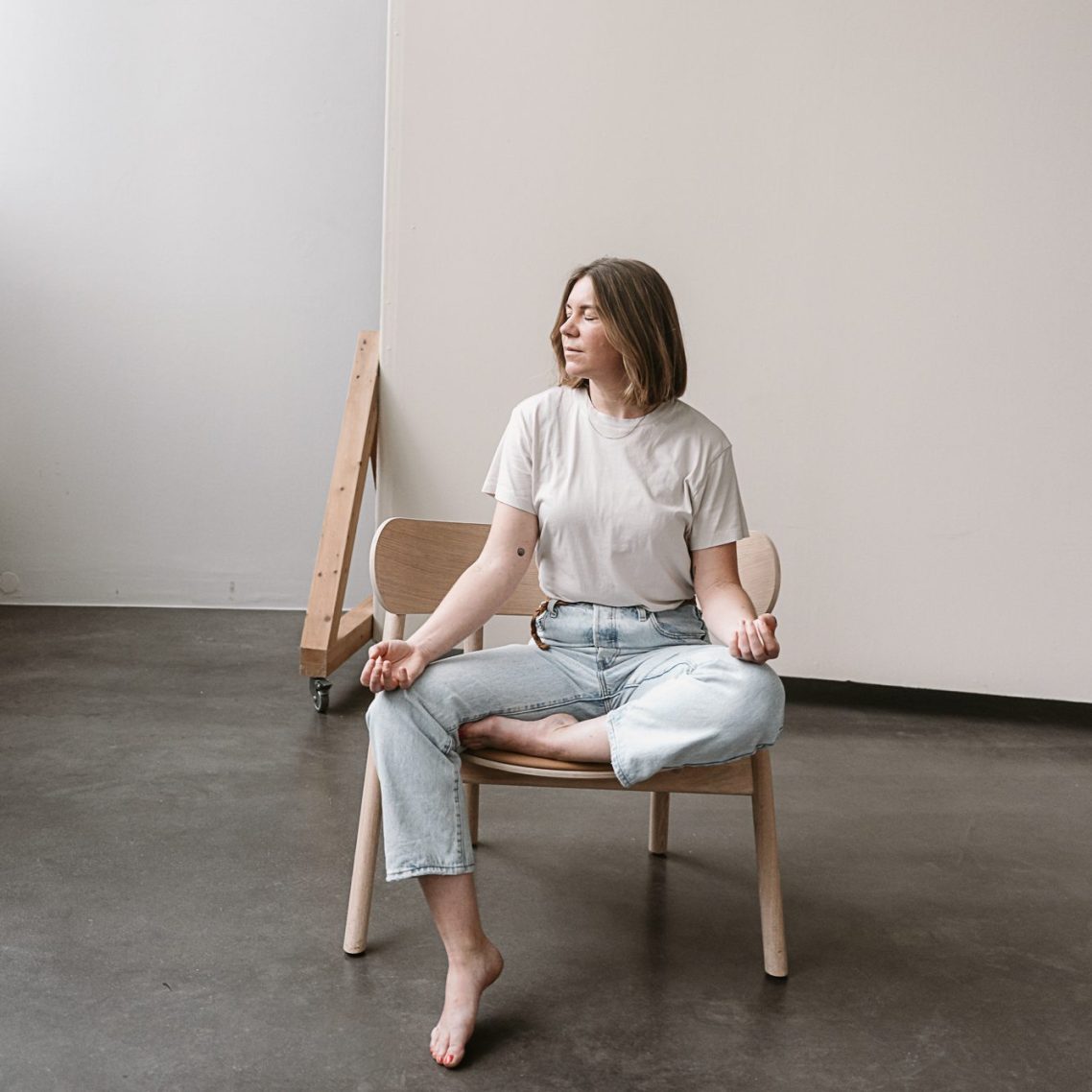 Eine Person sitzt in Meditierender Haltung auf einem Stuhl. Sie sieht fröhlich und gelassen aus.